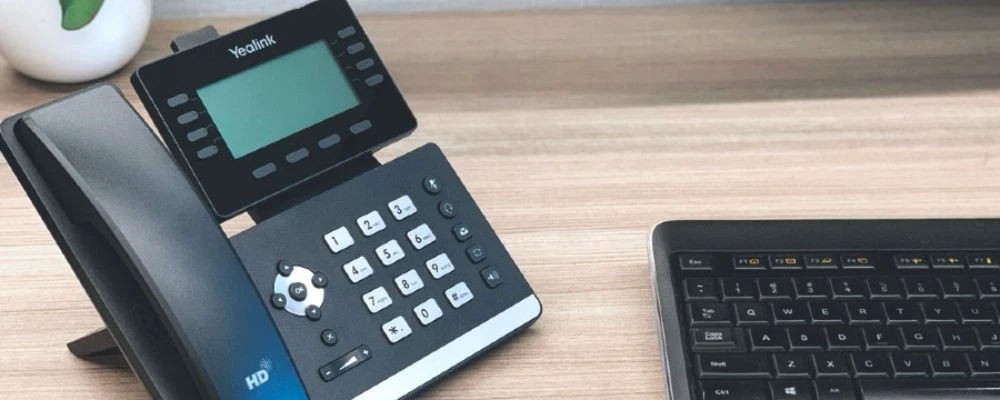 Yealink business IP desk phone on an office desk beside a keyboard.