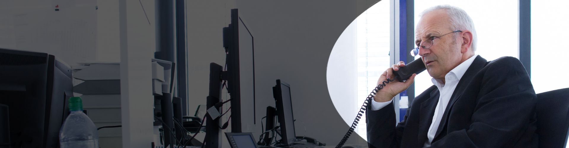 a finance director, seated at his desk, wearing a black suit and glasses, taking a call on finance business phone system