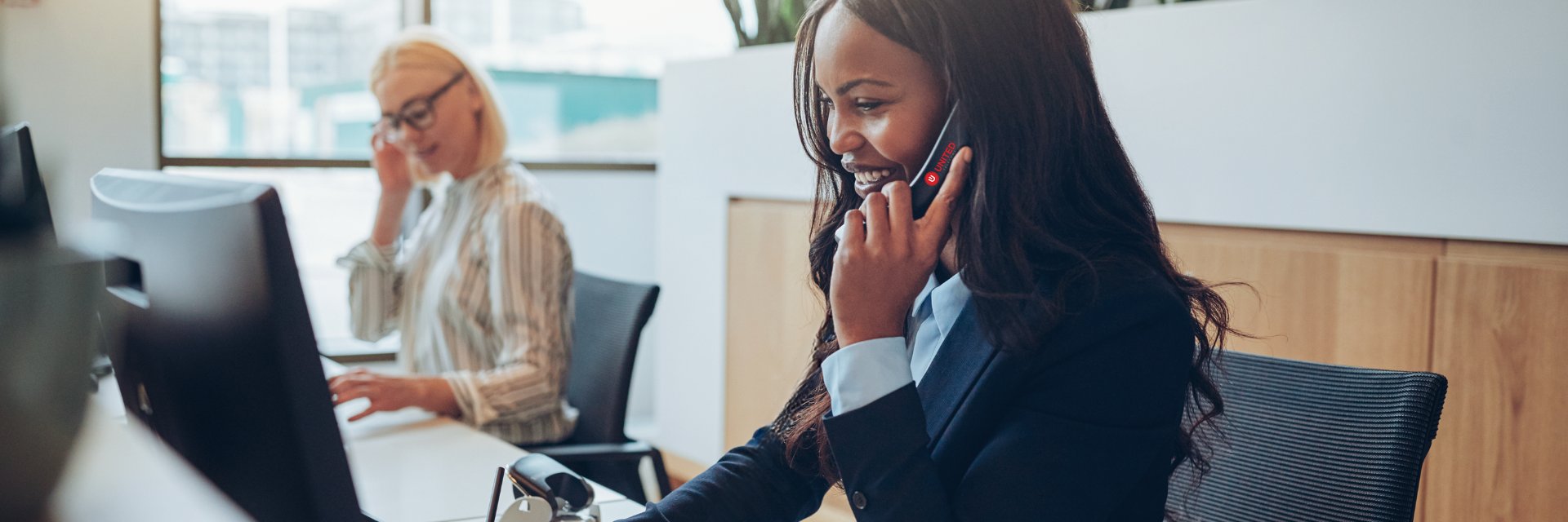 Young professional black women, seated at her desk, speaking with a client on her cordless VoIP phone