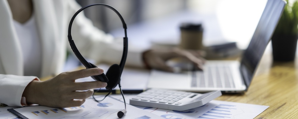 A businesswoman holding a headset analyses the cost of a Cloud PBX.