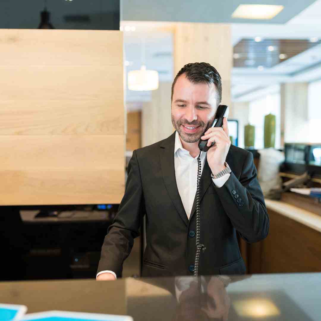 Hotel receptionist in a black suit using a Fanvil phone