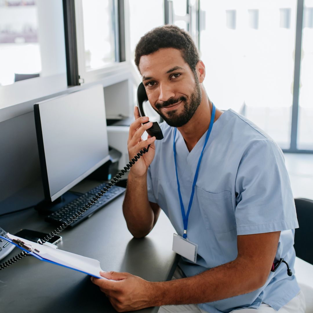 Healthcare worker answering a call on a desk phone at a medical practice.