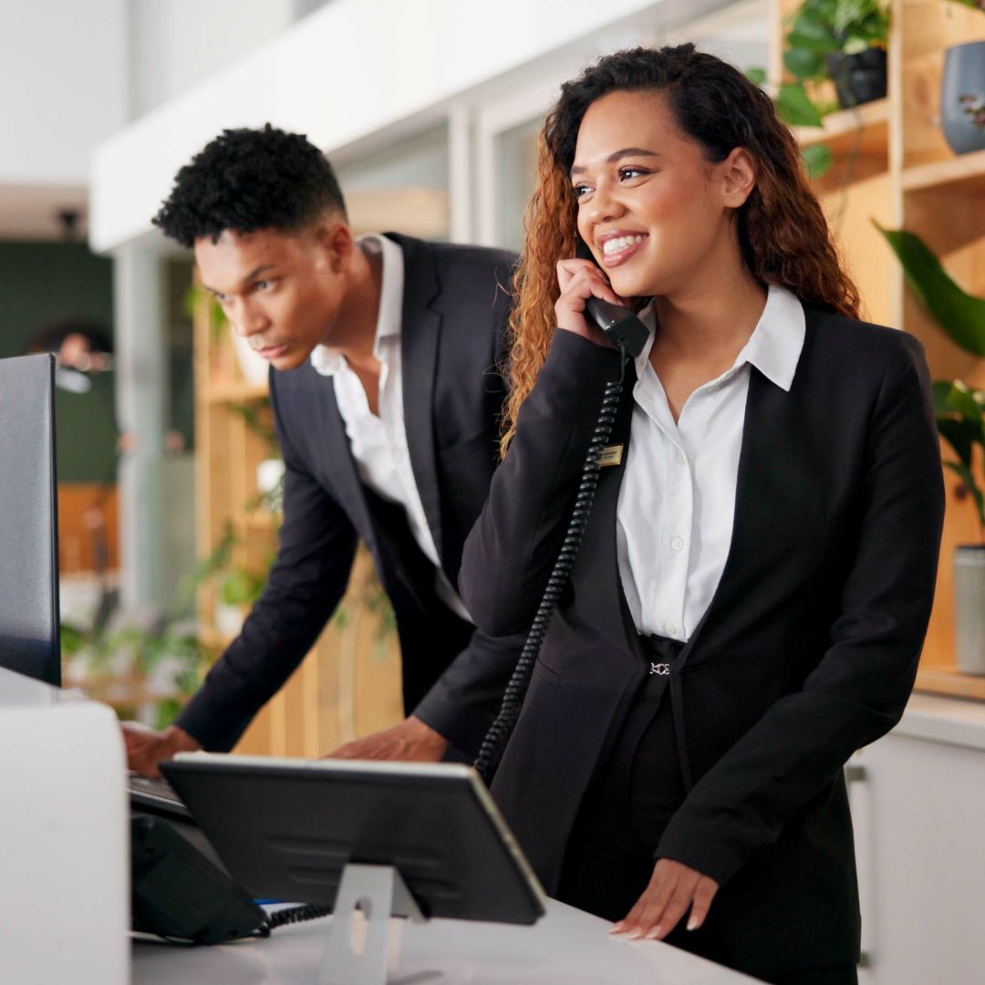 Hotel reception staff taking a guest call on a desk phone.