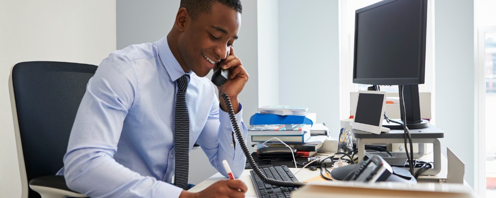A young business man wearing a blue shirt speaking with a client using a SIP-enabled telephone