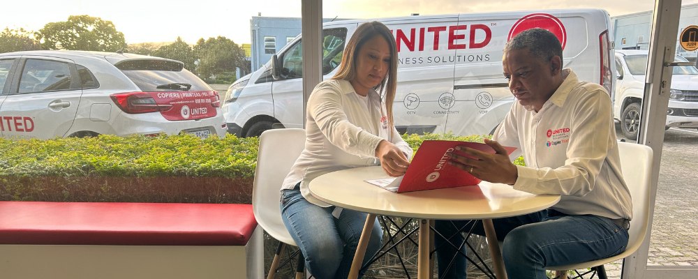 Two United Telecoms PBX phone system specialists seated at a table reviewing the company's catalogue.