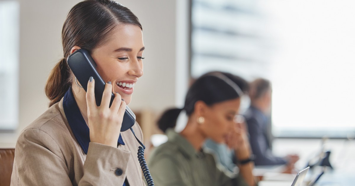A woman smiling and using a SIP-enabled deskphone