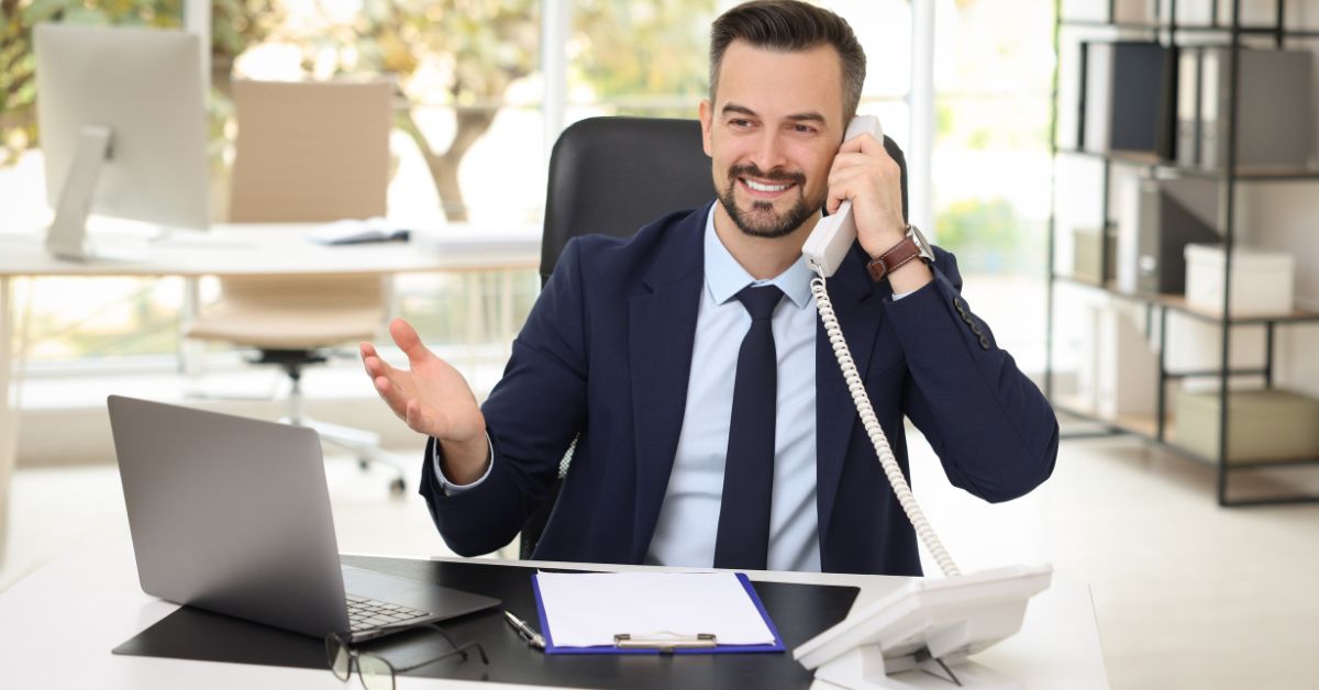 an insurance broker in a suit, speaking with a client on a business phone system