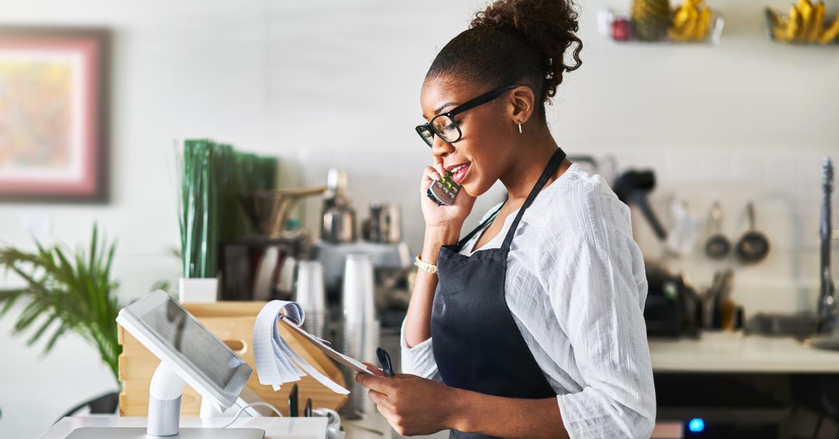A black woman standing at a pay point using a cordless VoIP phone at the front of her shop