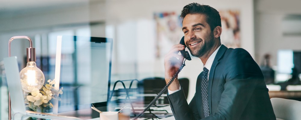 A businessman in his office using a desk phone to chat to a client.